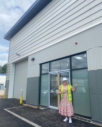 Photo of Laura wearing a hard hat and hi-vis jacket outside of a new works unit.